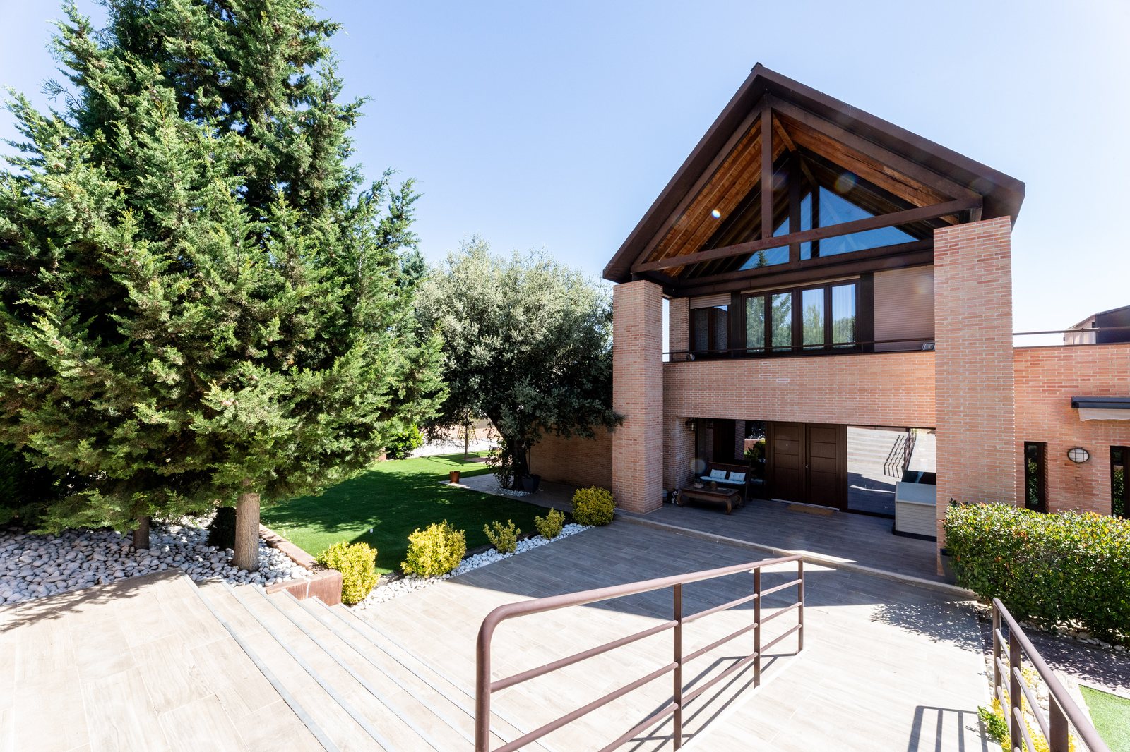 Fachada principal con pórtico triangular de madera, ladrillo visto y jardín
