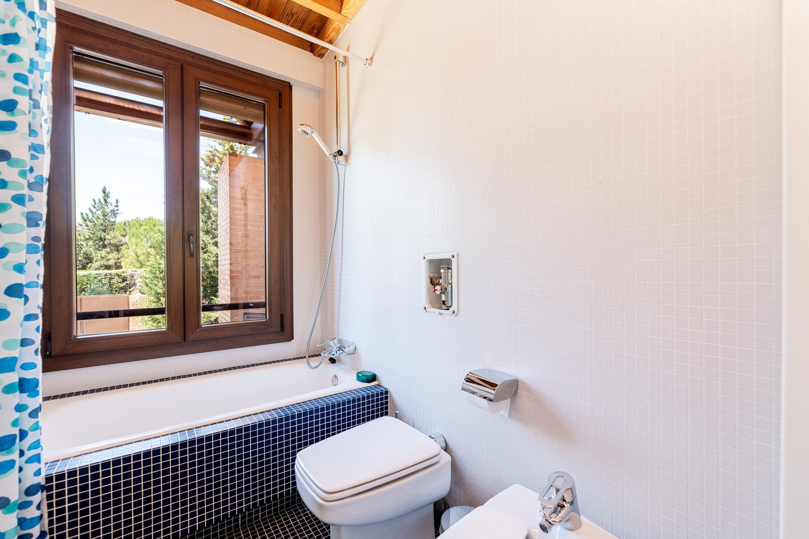 Baño con mosaico, ventana de madera y vista al jardín