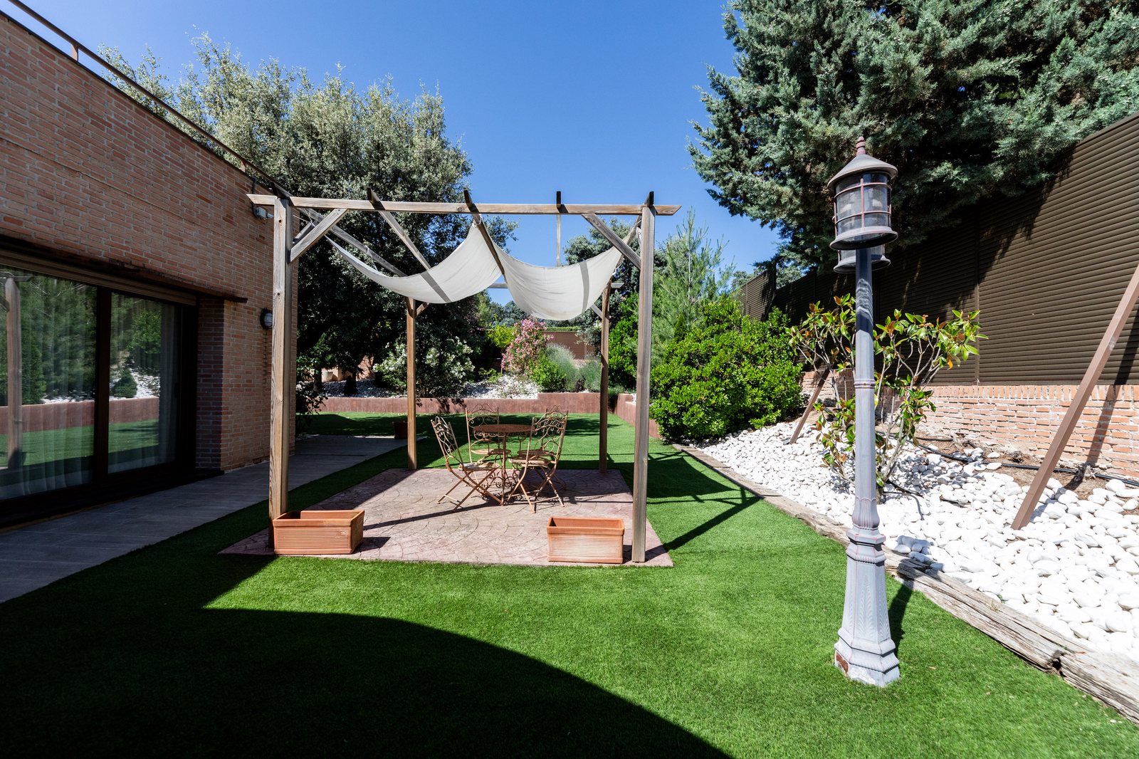 Jardín con pérgola y zona de estar exterior sobre césped
